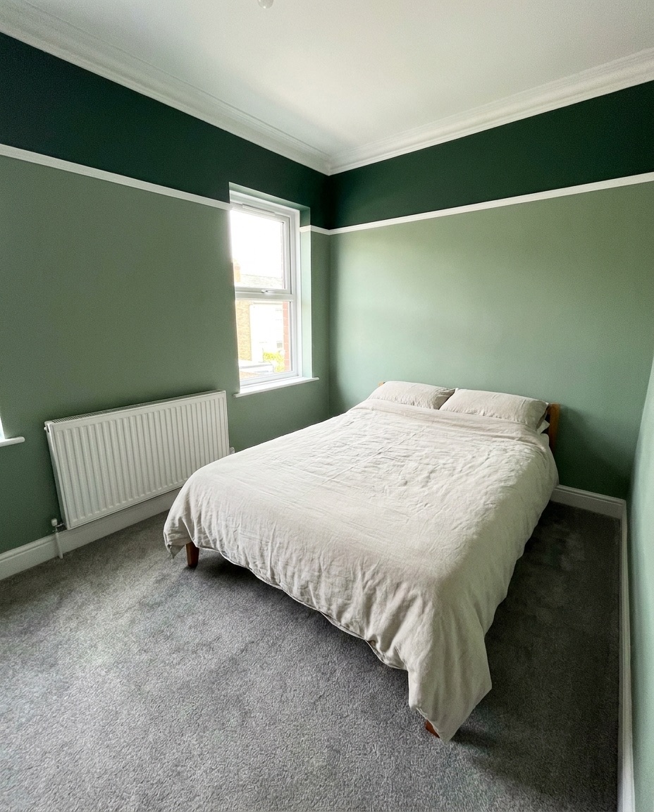 A bedroom painted in two tones of green with crisp white coving