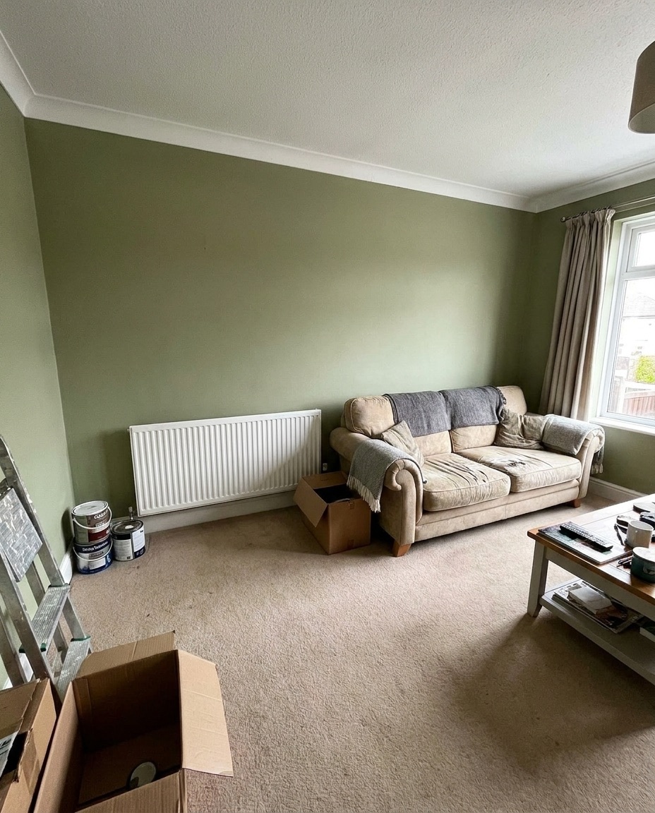 A living room freshly painted sage green with a white radiator under the window