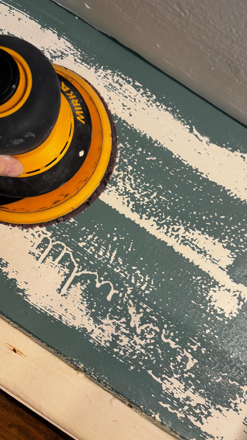 An orbital sander mid-prep on a teal painted panel